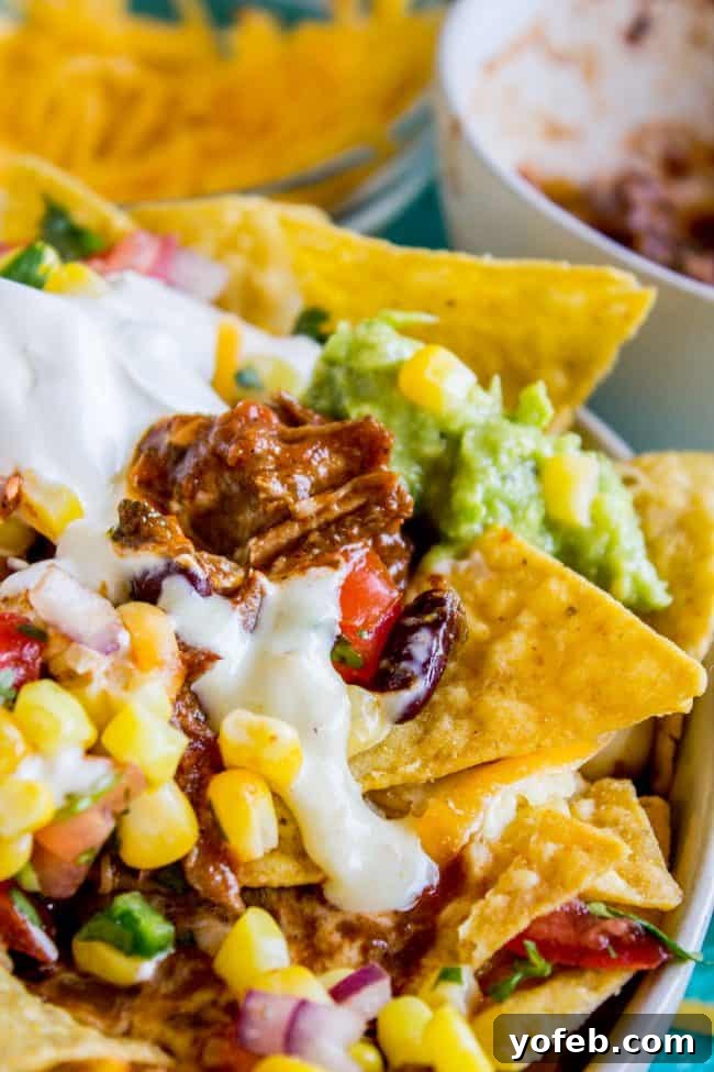 Stacked Chili Nachos with Molten Queso and Fresh Guacamole 10 A close-up of chili nachos loaded with shredded meat, sour cream, guacamole, melted cheese, corn, diced tomatoes, red onions, and cilantro.