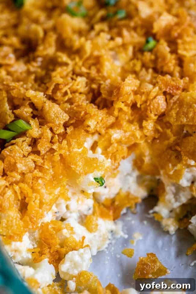 Funeral Potatoes (Cheesy Potato Casserole) from The Food Charlatan. If you haven't heard of this side dish, you will love it! Potatoes mixed with sour cream, butter, white sauce (or a can of soup - I include instructions for both), and tons of cheddar cheese, then baked to perfection with a crunchy corn flake topping. It doesn't get any better for holidays! #potatoes #withhashbrowns #easy #casserole #baked #cornflakes #fromscratch #withcornflakes #inoven #soup #homemade #quick #best cheesy potatoes topped with cornflakes in a pan with a serving missing.