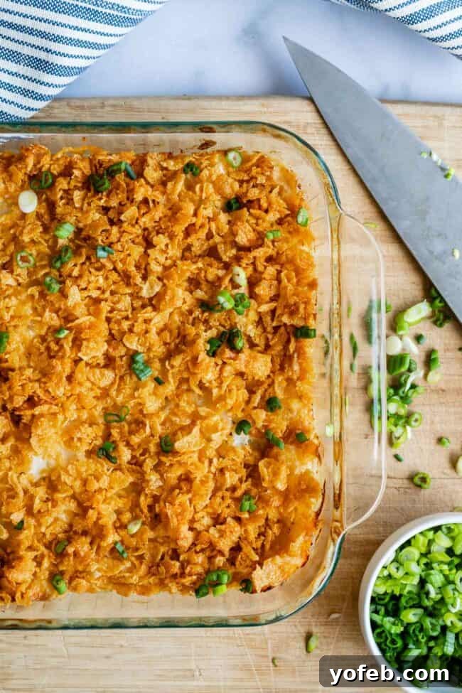 Funeral Potatoes (Cheesy Potato Casserole) from The Food Charlatan. If you haven't heard of this side dish, you will love it! Potatoes mixed with sour cream, butter, white sauce (or a can of soup - I include instructions for both), and tons of cheddar cheese, then baked to perfection with a crunchy corn flake topping. It doesn't get any better for holidays! #potatoes #withhashbrowns #easy #casserole #baked #cornflakes #fromscratch #withcornflakes #inoven #soup #homemade #quick #best funeral potatoes in a clear glass dish shot from overhead, with green onions and chef's knife.