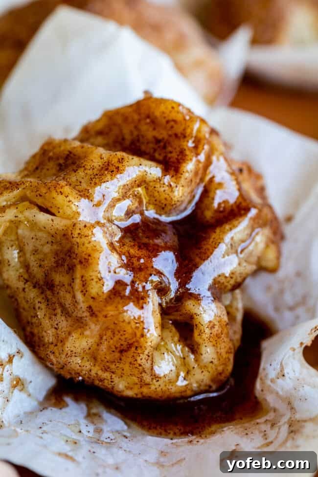 Miracle Easter Rolls 3 A close-up of a baked apple dumpling, reminiscent of resurrection rolls, topped with glossy brown cinnamon sugar syrup and resting on crinkled parchment paper.
