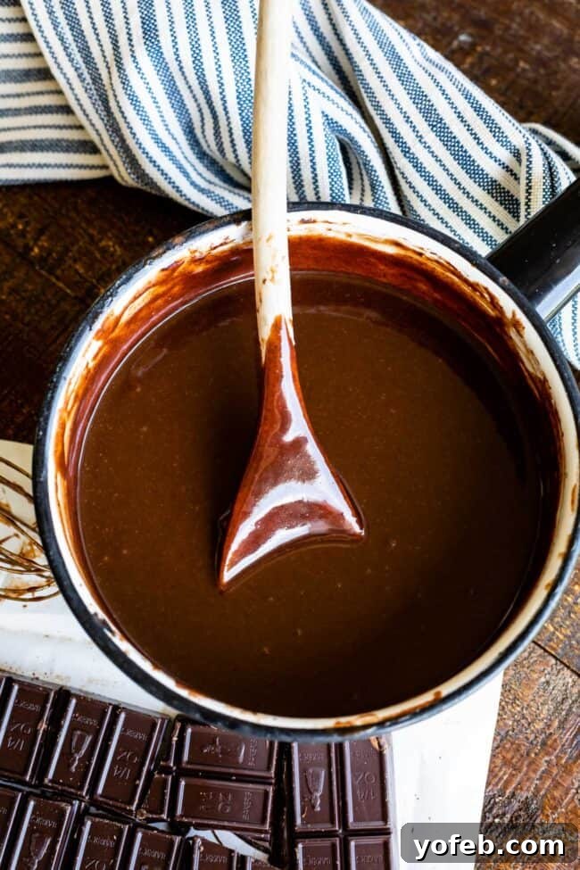 Easy Homemade Chocolate Sauce 3 A wooden spoon rests in a pot of freshly made, glossy hot fudge sauce, ready to be served.