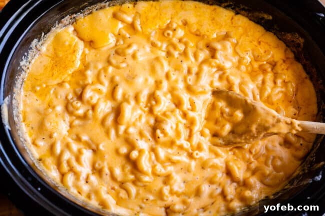 Overhead shot of the finished slow cooker mac and cheese in the pot with a wooden spoon, perfectly creamy and ready to serve.