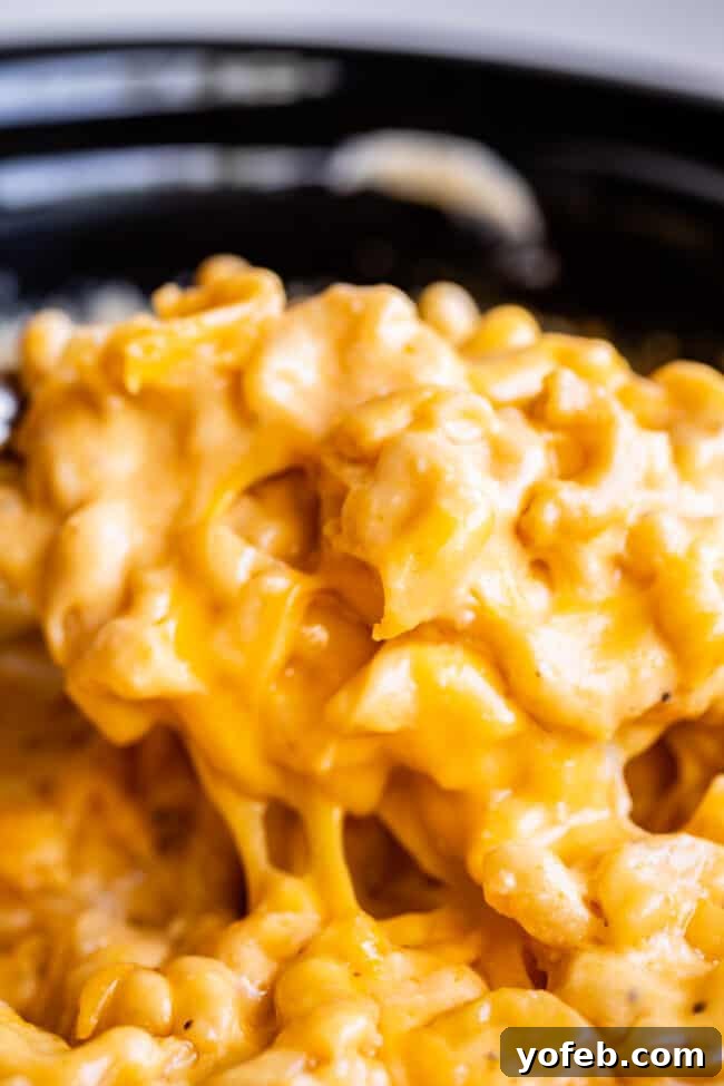 Mac and cheese in the slow cooker being lifted with a serving spoon, creating an impressive cheese pull from the added slices.