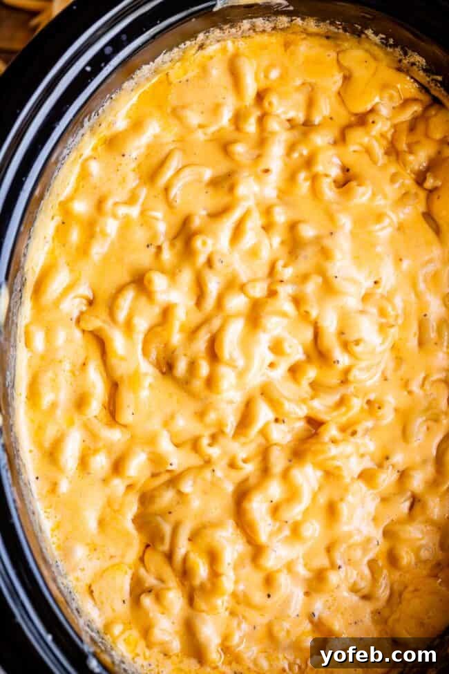 Overhead shot of rich, golden slow cooker mac and cheese bubbling in a black crockpot, ready to serve.