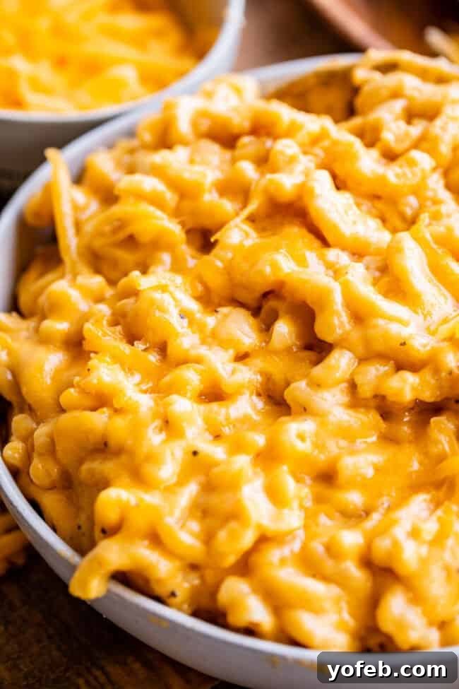 A white serving bowl generously filled with slow-cooked mac and cheese, generously topped with shredded cheddar cheese, inviting a delicious bite.
