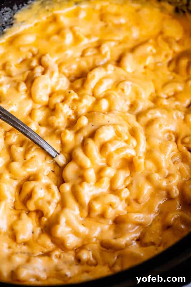 Slow-cooked mac and cheese in a black crock pot with a serving spoon nestled within, inviting a taste.