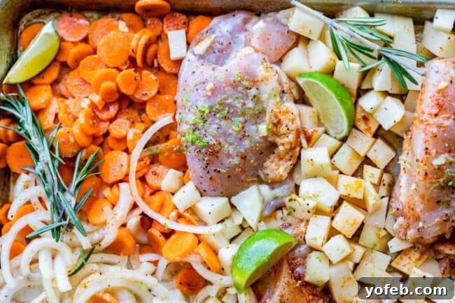Sheet Pan Rosemary Lime Chicken and Veggies Delicious baked rosemary chicken thigh resting on a bed of roasted vegetables on a sheet pan.