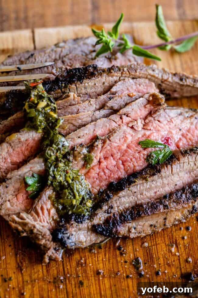 How to Cook Flank Steak (Grilled or Oven Broiled) A beautifully cooked flank steak resting on a wooden cutting board, ready to be sliced, accompanied by a side of fresh chimichurri sauce.