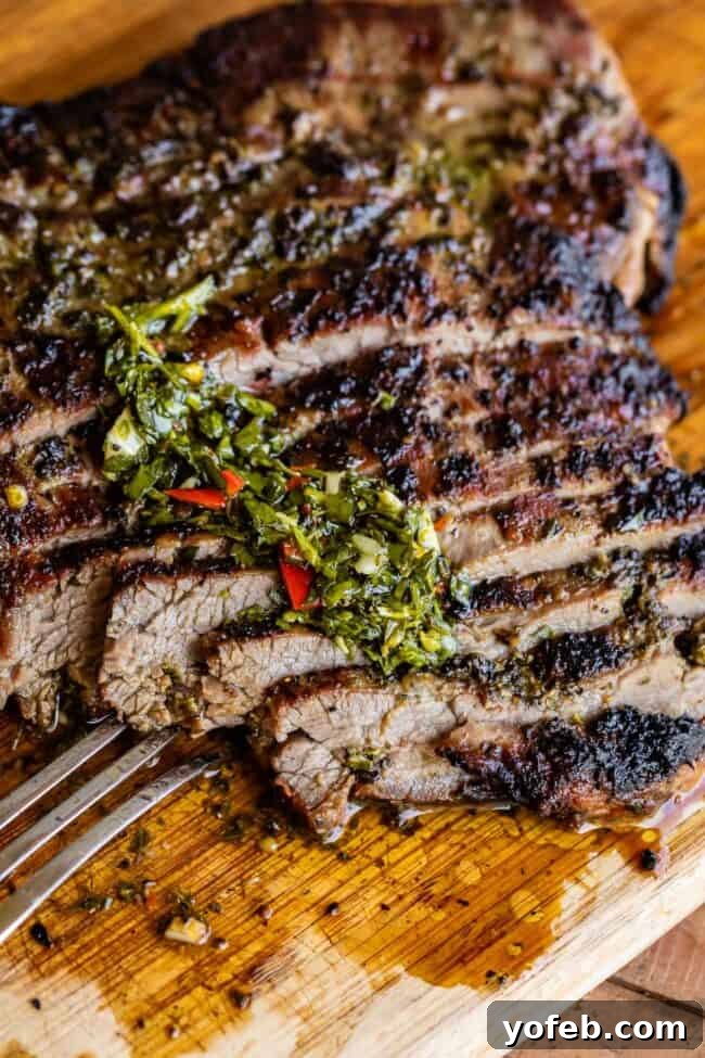 How to Cook Flank Steak (Grilled or Oven Broiled) Succulent grilled sliced flank steak on a wooden cutting board, garnished with fresh chimichurri sauce and a metal fork.