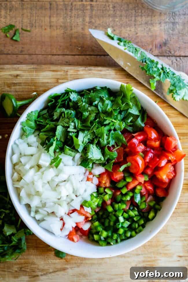 How to Make Authentic Pico de Gallo from The Food Charlatan. Learn how to make the best Pico de Gallo! It's a very simple Mexican salsa with tomatoes, onions, jalapeno, cilantro, and lime juice. Humble ingredients come together to make one of the best appetizers of all time! You will never look at tacos the same after topping them with this magical stuff. #picodegallo #salsa #Mexican #cold #fresh #appetizer #dip #forparties #easy #recipe #receta #authentic #best #homemade #restaurant #picodegalo pico de gallo ingredients in a white bowl with a wooden cutting board and knife. A vibrant medley of chopped tomatoes, onions, jalapeños, and cilantro in a white bowl, ready to be seasoned and mixed for pico de gallo.