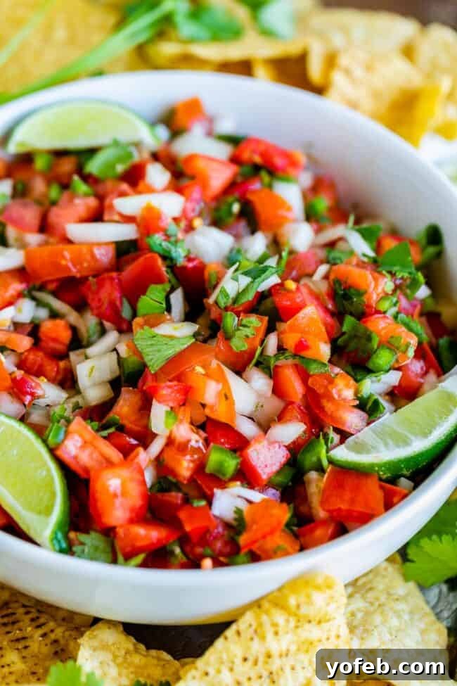 How to Make Authentic Pico de Gallo from The Food Charlatan. Learn how to make the best Pico de Gallo! It's a very simple Mexican salsa with tomatoes, onions, jalapeno, cilantro, and lime juice. Humble ingredients come together to make one of the best appetizers of all time! You will never look at tacos the same after topping them with this magical stuff. #picodegallo #salsa #Mexican #cold #fresh #appetizer #dip #forparties #easy #recipe #receta #authentic #best #homemade #restaurant #picodegalo pico de gallo with lime wedges and tortilla chips. A fresh bowl of pico de gallo, artfully arranged with lime wedges and crispy tortilla chips, epitomizing a perfect snack or appetizer.