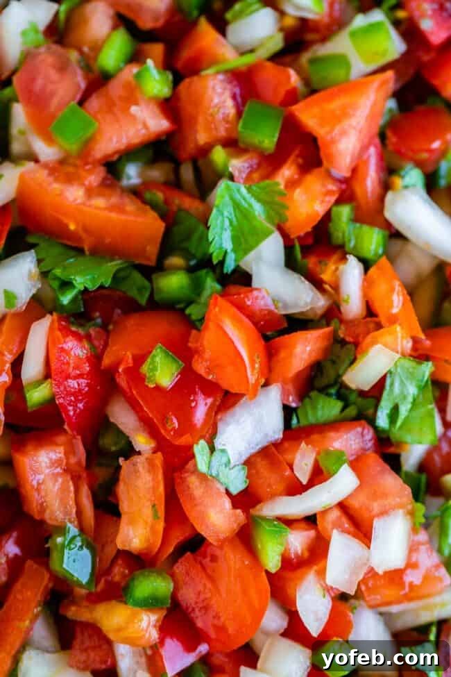 How to Make Authentic Pico de Gallo from The Food Charlatan. Learn how to make the best Pico de Gallo! It's a very simple Mexican salsa with tomatoes, onions, jalapeno, cilantro, and lime juice. Humble ingredients come together to make one of the best appetizers of all time! You will never look at tacos the same after topping them with this magical stuff. #picodegallo #salsa #Mexican #cold #fresh #appetizer #dip #forparties #easy #recipe #receta #authentic #best #homemade #restaurant #picodegalo homemade pico de gallo. A close-up shot of homemade pico de gallo, showcasing the fresh, chunky vegetables and vibrant colors.
