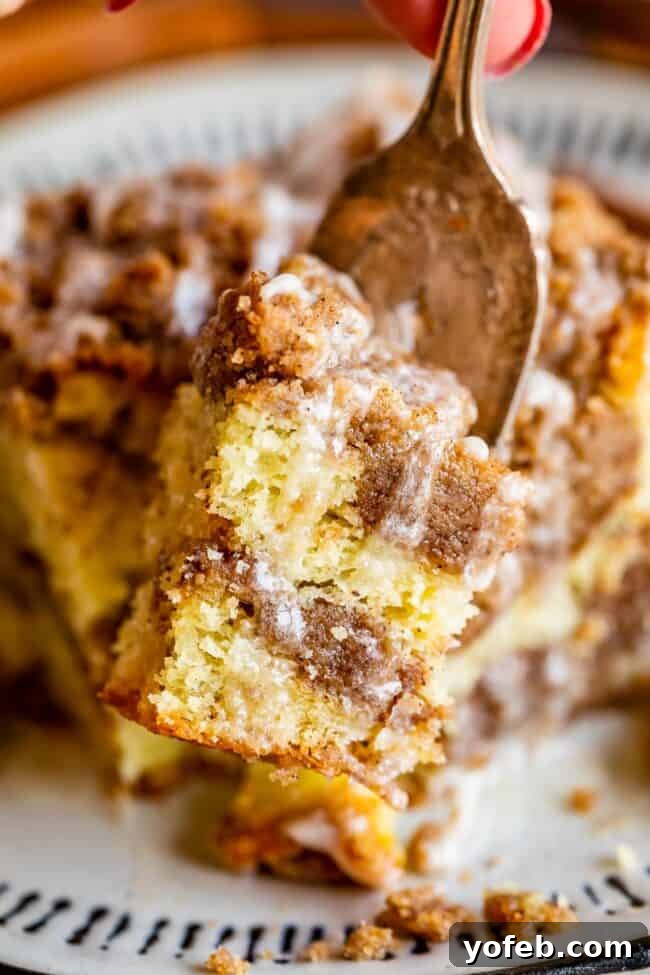 Sour Cream Coffee Cake, with a Ridiculous Amount of Streusel from The Food Charlatan. This is my FAVORITE recipe for Sour Cream Coffee Cake! My main complaint with Coffee Cake is that there is usually too much cake, not enough streusel. This recipe gives you the max amount of streusel without ruining the light fluffiness of the cake! A vanilla drizzle finishes it off! #coffeecake #sourcream #icing #frosting #drizzle #easy #recipes #cinnamon #streusel #sourcream #crumb #crumble #moist #breakfast Slice of coffee cake with streusel and glaze on a fork.