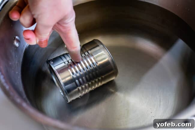 A can of sweetened condensed milk being carefully placed into a pot of water on the stovetop for making dulce de leche.