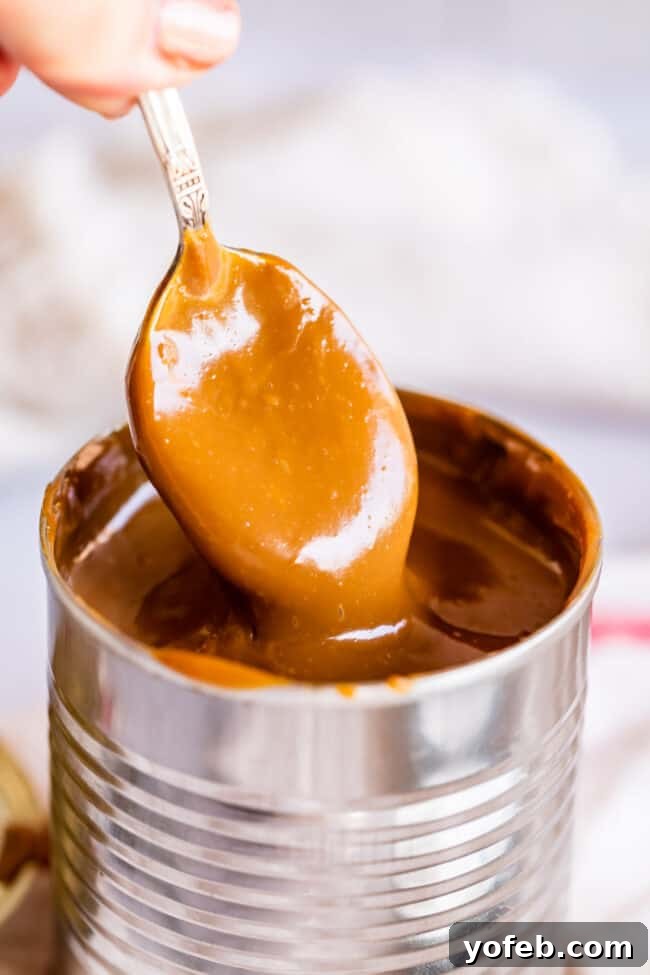 A spoonful of homemade dulce de leche being lifted from a can, showcasing its smooth, glossy texture and inviting golden-brown hue.