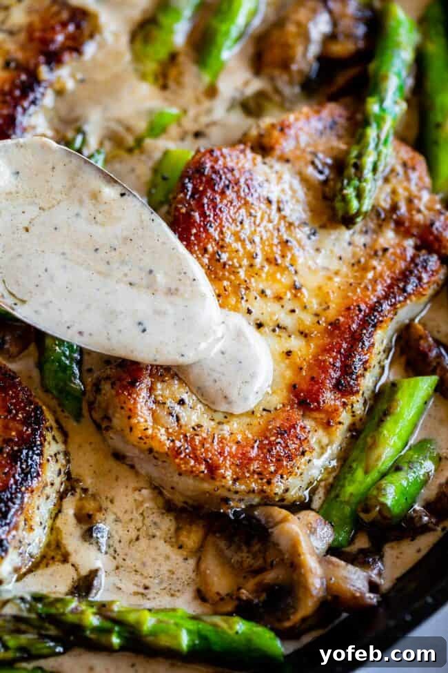 Pan-Seared Pork Chops with Velvety Mushroom Sauce 5 A serving of perfectly seared pork chop with a rich, creamy gravy being spooned over fresh asparagus and sautéed mushrooms, highlighting the delicious textures and flavors.