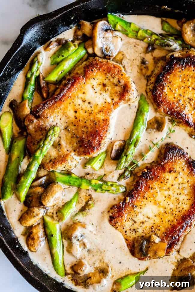 Pan-Seared Pork Chops with Velvety Mushroom Sauce 6 A hearty portion of seared boneless pork chops nestled amidst vibrant green asparagus, golden-brown mushrooms, and fresh sprigs of thyme, all swimming in a creamy, savory gravy within a robust cast iron skillet.