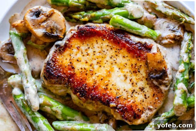 Pan-Seared Pork Chops with Velvety Mushroom Sauce 9 A close-up of a single seared pork chop, generously draped in a rich, creamy gravy, surrounded by tender sautéed mushrooms and vibrant asparagus spears, ready to be enjoyed.