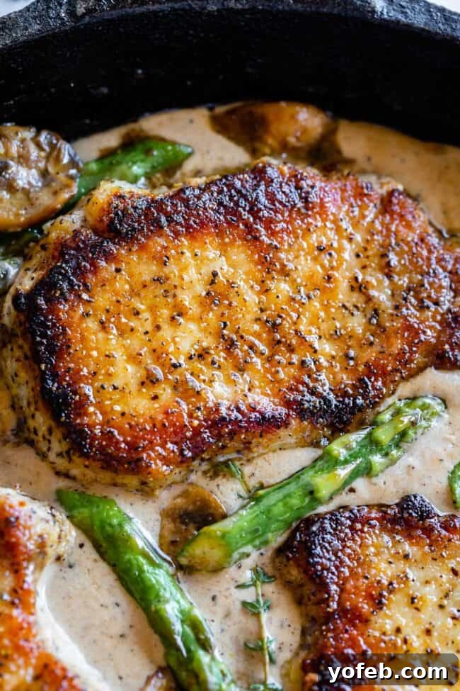 Pan-Seared Pork Chops with Velvety Mushroom Sauce 10 A close-up shot of a perfectly seared pork chop, generously covered in a creamy pan sauce, accompanied by tender sautéed mushrooms, vibrant asparagus, and garnished with fresh thyme sprigs in a skillet.