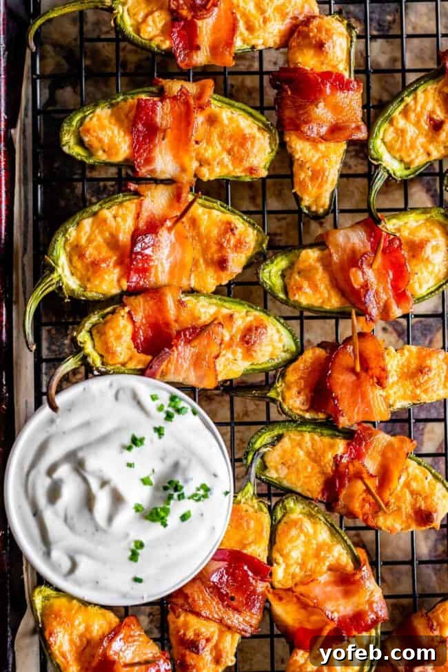 Bacon Wrapped Jalapeño Poppers with Creamy Ranch Dip A close-up of a perfectly baked bacon-wrapped jalapeño popper being dipped into a bowl of creamy ranch dressing, emphasizing its crispy texture.