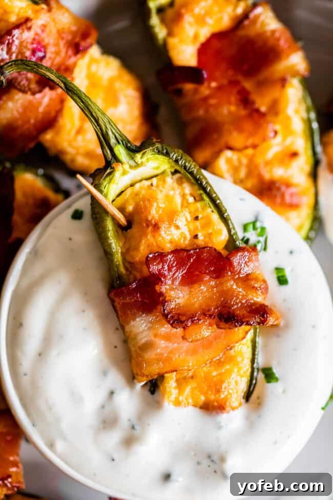Bacon Jalapeño Popper with Ranch Dip A single, golden-crisp bacon-wrapped jalapeño popper being dipped into a small bowl of creamy ranch dressing, ready to be enjoyed.
