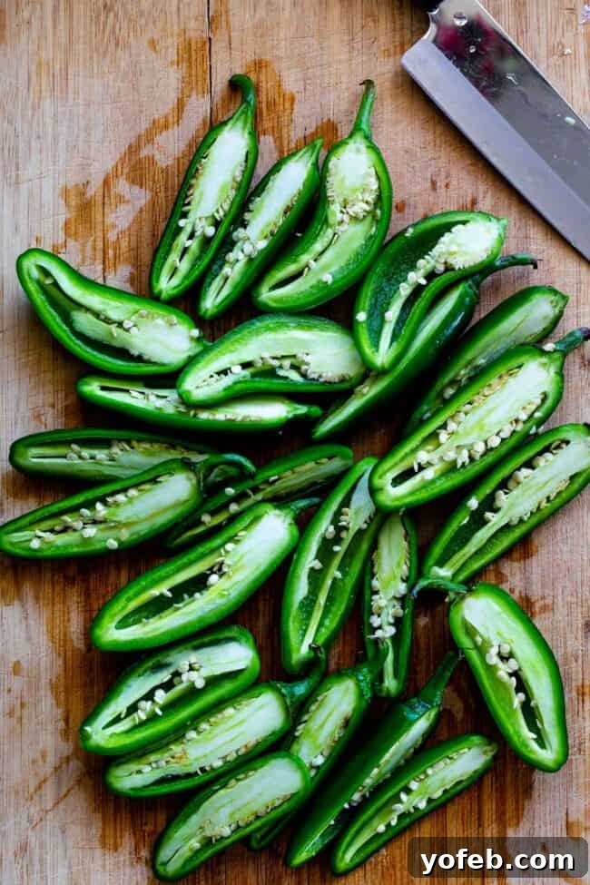 Jalapeños Sliced in Half for Poppers Fresh green jalapeños sliced cleanly in half lengthwise on a rustic wooden cutting board, with stems intact.