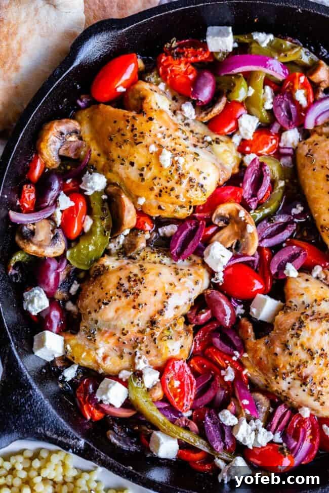 One-Pan Zesty Greek Chicken and Roasted Vegetables 2 Golden brown oven baked Greek chicken thighs with vibrant bell peppers, red onion, mushrooms, and cherry tomatoes in a cast iron skillet, garnished with Kalamata olives and feta cheese.