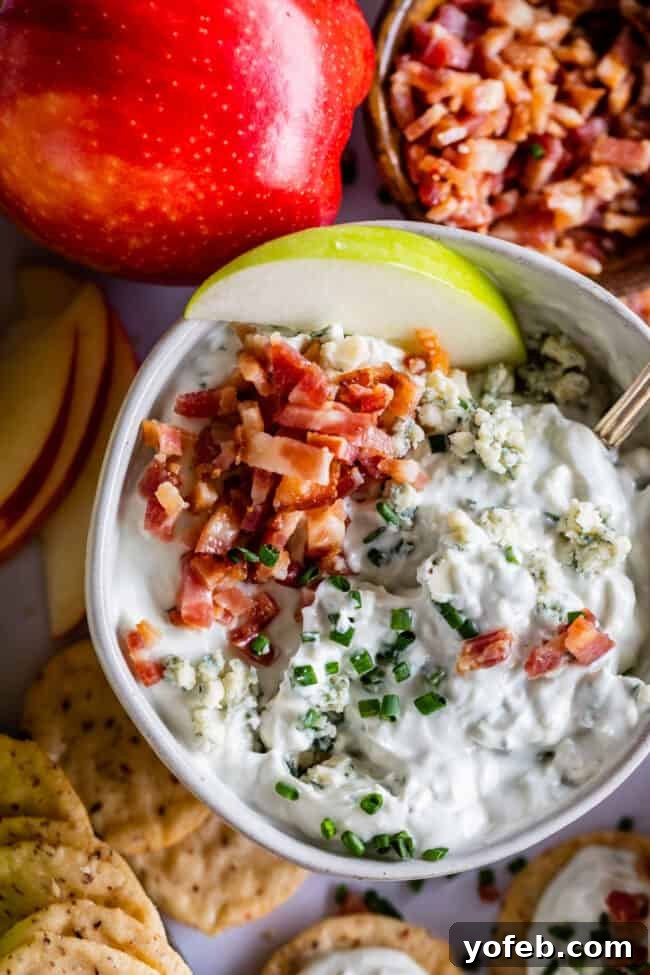 Easy Homemade Blue Cheese Dip with Bacon and Chives Bowl of blue cheese dip surrounded by fresh ingredients like chives and more blue cheese, emphasizing homemade quality.
