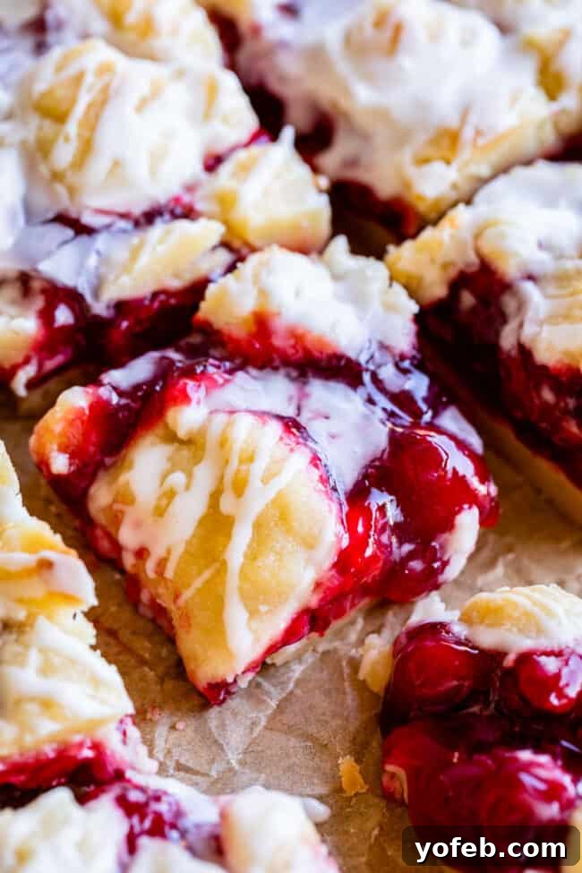 A trio of homemade cherry pie bars, displaying their inviting layers of crust, filling, and glaze, arranged on a light background.