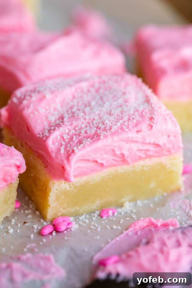 The secret is in the cream cheese. It doesn't go in the frosting! It replaces some of the butter usually called for in the sugar cookies. The cream cheese makes the final baked cookie supremely chewy and moist. sugar cookie bars topped with pink frosting and sprinkles on a cooling rack
