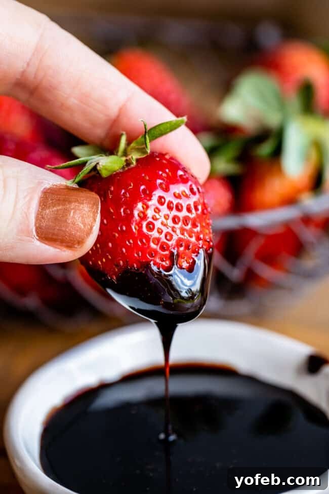 Strawberry with Balsamic Glaze A hand dipping a vibrant red strawberry into a rich, dark balsamic vinegar reduction, showcasing its syrupy consistency.