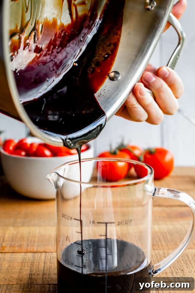 Transferring Homemade Balsamic Glaze to Storage Pouring the finished balsamic reduction from a metal pan into a glass measuring cup, with ripe tomatoes in the background.