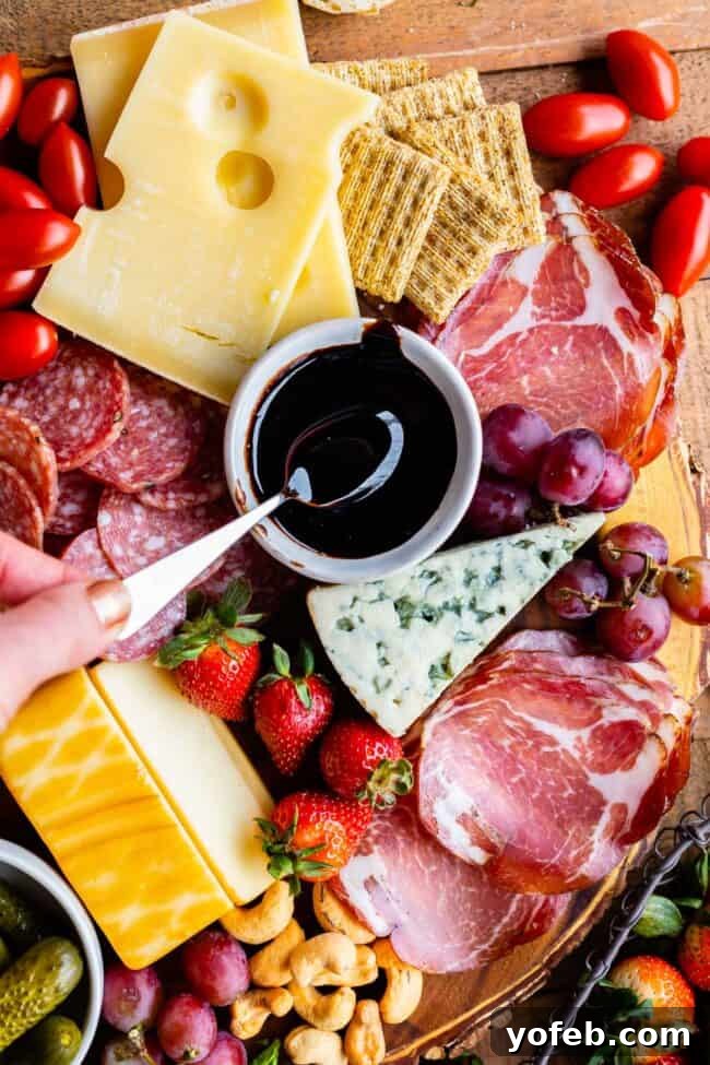 Balsamic Glaze on a Charcuterie Board Balsamic reduction glaze drizzled artfully on a wooden charcuterie board featuring prosciutto, various cheeses, crackers, fresh fruits, nuts, and cherry tomatoes.
