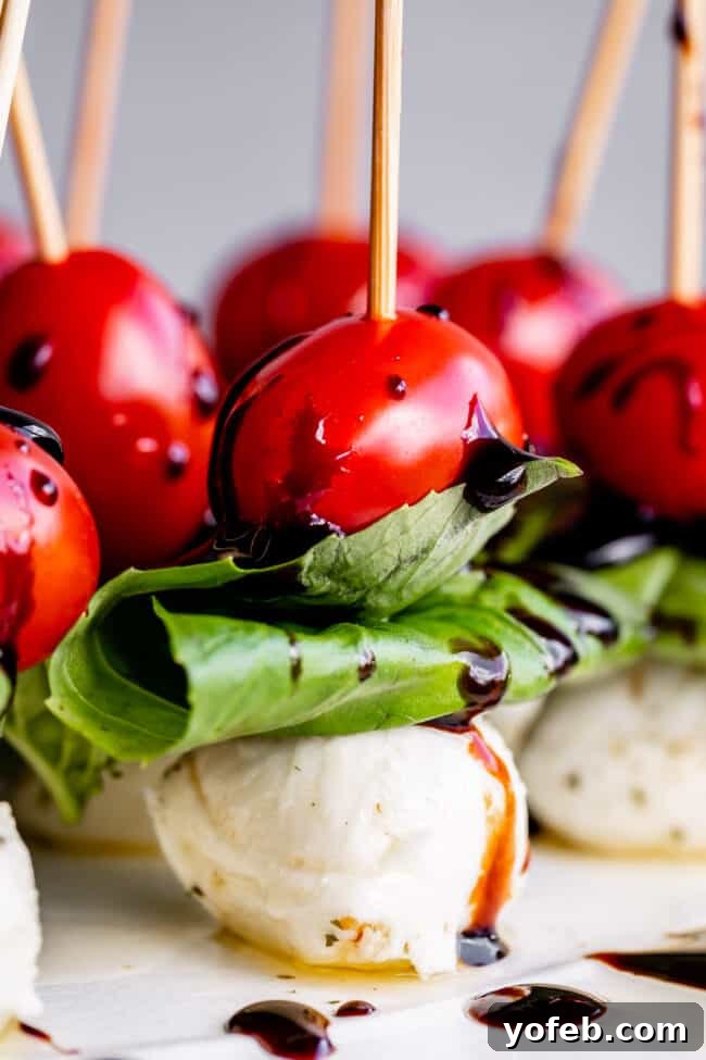 Caprese Salad Skewers Appetizer Caprese Salad Skewers Appetizer - vibrant cherry tomatoes, fresh basil, and marinated mozzarella drizzled with balsamic glaze, served on a platter.