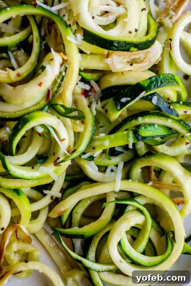 Spiralizer-Free Zucchini Noodles 2 Close-up shot of perfectly curly zucchini noodles topped with grated cheese, showcasing their appetizing texture.