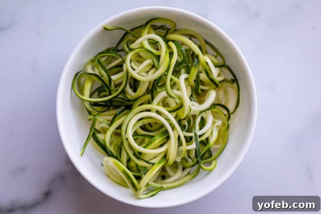 Spiralizer-Free Zucchini Noodles 11 A white bowl brimming with fresh zucchini noodles, shot from an overhead perspective on a kitchen countertop.