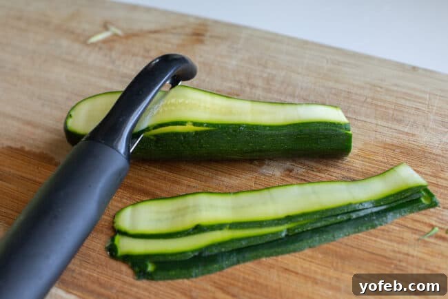 Spiralizer-Free Zucchini Noodles 12 A vegetable peeler skillfully transforming a zucchini into delicate, flat ribbons on a cutting board.