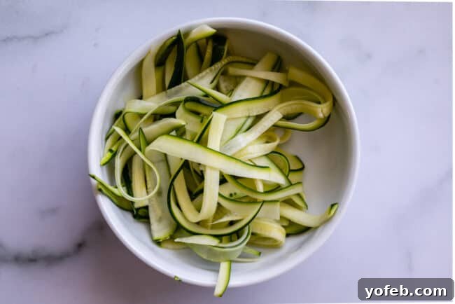 Spiralizer-Free Zucchini Noodles 13 A bowl filled with thin, flat zucchini ribbons, created using a simple vegetable peeler, on a kitchen surface.