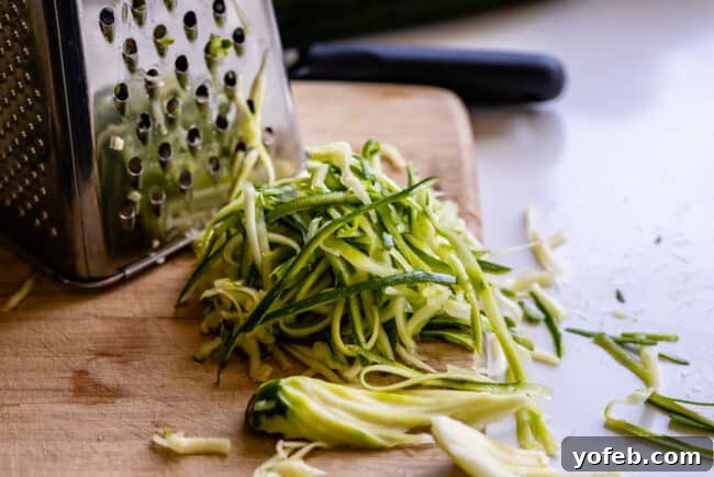Spiralizer-Free Zucchini Noodles 14 A box grater actively being used to transform a zucchini into thin, spaghetti-like strands.