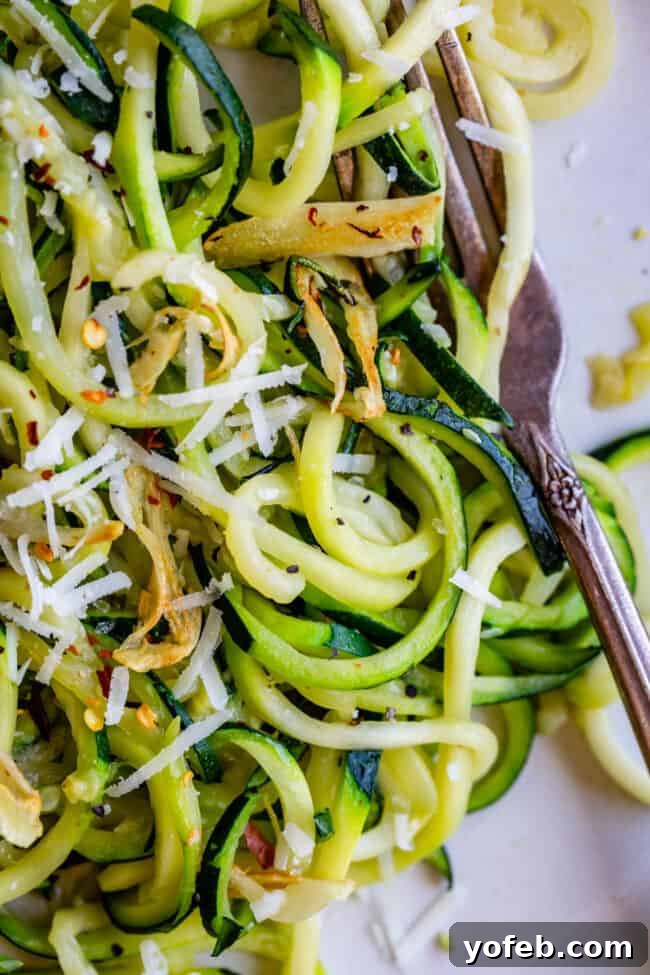 Spiralizer-Free Zucchini Noodles 17 A fork piercing through a tangle of zucchini noodles, garnished with red pepper flakes, highlighting their firm texture.