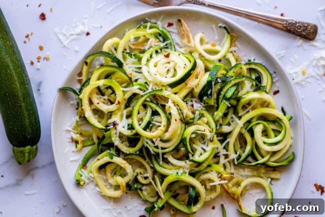 Spiralizer-Free Zucchini Noodles 19 A white plate holding a serving of zucchini noodles, with a fork resting beside them.