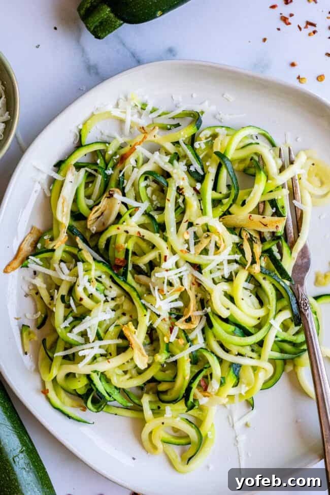 Spiralizer-Free Zucchini Noodles 4 Overhead view of vibrant zucchini noodles on a white plate, garnished with cheese and a sprinkle of herbs.