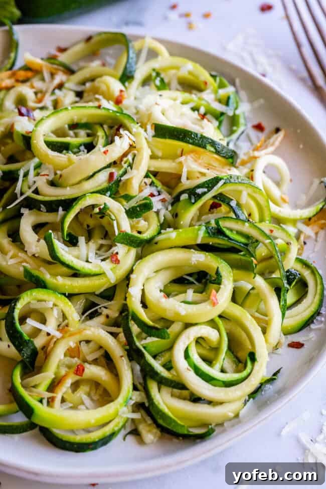 Spiralizer-Free Zucchini Noodles 5 Curly zucchini noodles arranged on a white plate, topped with grated Parmesan and red pepper flakes for a touch of spice.