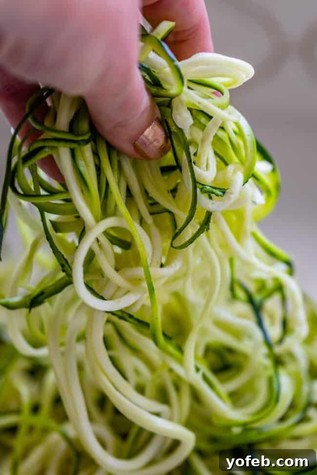 Spiralizer-Free Zucchini Noodles 6 A hand gently lifting a tangle of zucchini noodles from a kitchen countertop, ready for cooking.