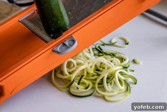 Spiralizer-Free Zucchini Noodles 9 Illustrating the twisting technique on a mandoline to produce curly zucchini noodles, showing hands in action.