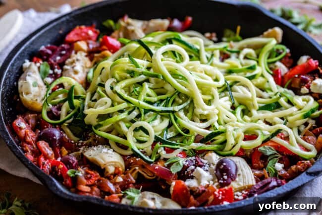 Zoodles Mixed with Greek Chicken and Veggies Cooked zoodles tossed lightly with the Greek chicken and vegetable mixture in a pan, offering a healthy and low-carb option for the Mediterranean dish.