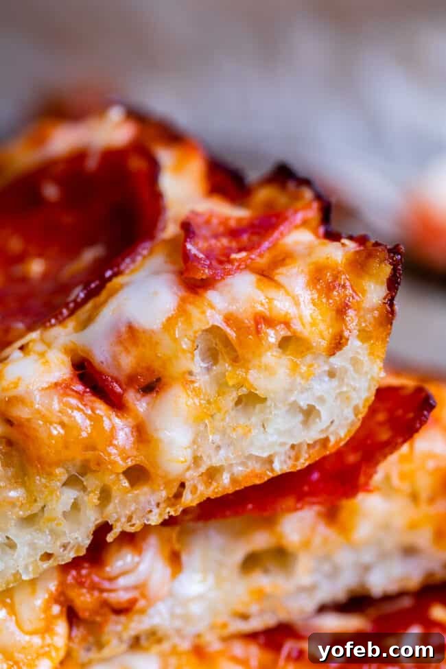 Multiple slices of homemade pan pizza stacked neatly, revealing the inviting thickness and texture of the crust.