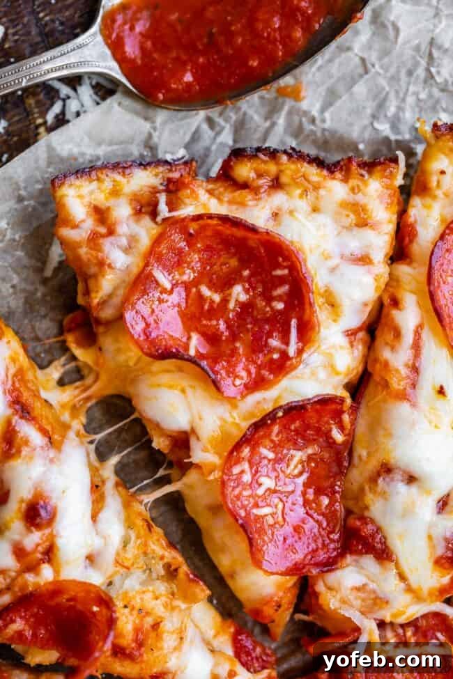 A delectable slice of pizza with a perfectly crispy crust, artfully arranged next to other slices featuring enticingly stretchy cheese, all presented on wax paper alongside a spoon holding pizza sauce.