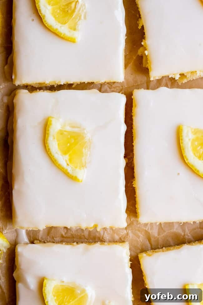 Lemon Sheet Cake with Lemon Glaze. This Lemon Sheet Cake with Lemon Glaze is perfect for lemon lovers! A supremely lemony and MOIST cake, paired with a bright lemon glaze. It is perfect for summertime, or anytime! This recipe feeds a crowd and is super easy to make. #lemon #cake #sheetcake #lemoncake #citrus #summer #easy #recipe #zest #tart #withglaze #fromscratch #homemade #glaze #best #Texas #simple #dessert #feedsacrowd #foracrowd squares of lemon sheet cake, glazed, with lemon slices.