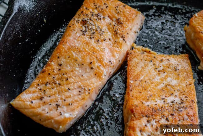 Creamy Tuscan Salmon (30 Minute Dinner!) from The Food Charlatan. This Creamy Tuscan Salmon recipe is totally restaurant quality, but super easy to make! Perfectly pan-seared salmon, drowning in a creamy parmesan sauce with garlic, cherry tomatoes, spinach, and fresh basil. It's the perfect summer meal and is done in 30 minutes! #easy #recipe #summer #garden #salmon #tuscan #creamy #cherrytomato #basil #spinach #parmesan #tomato #30minutedinner #oneskillet #garlic #butter #garlicbutter #pasta salmon fillets seasoned with salt and pepper being seared in a hot cast iron skillet, showing a beautiful brown crust forming.